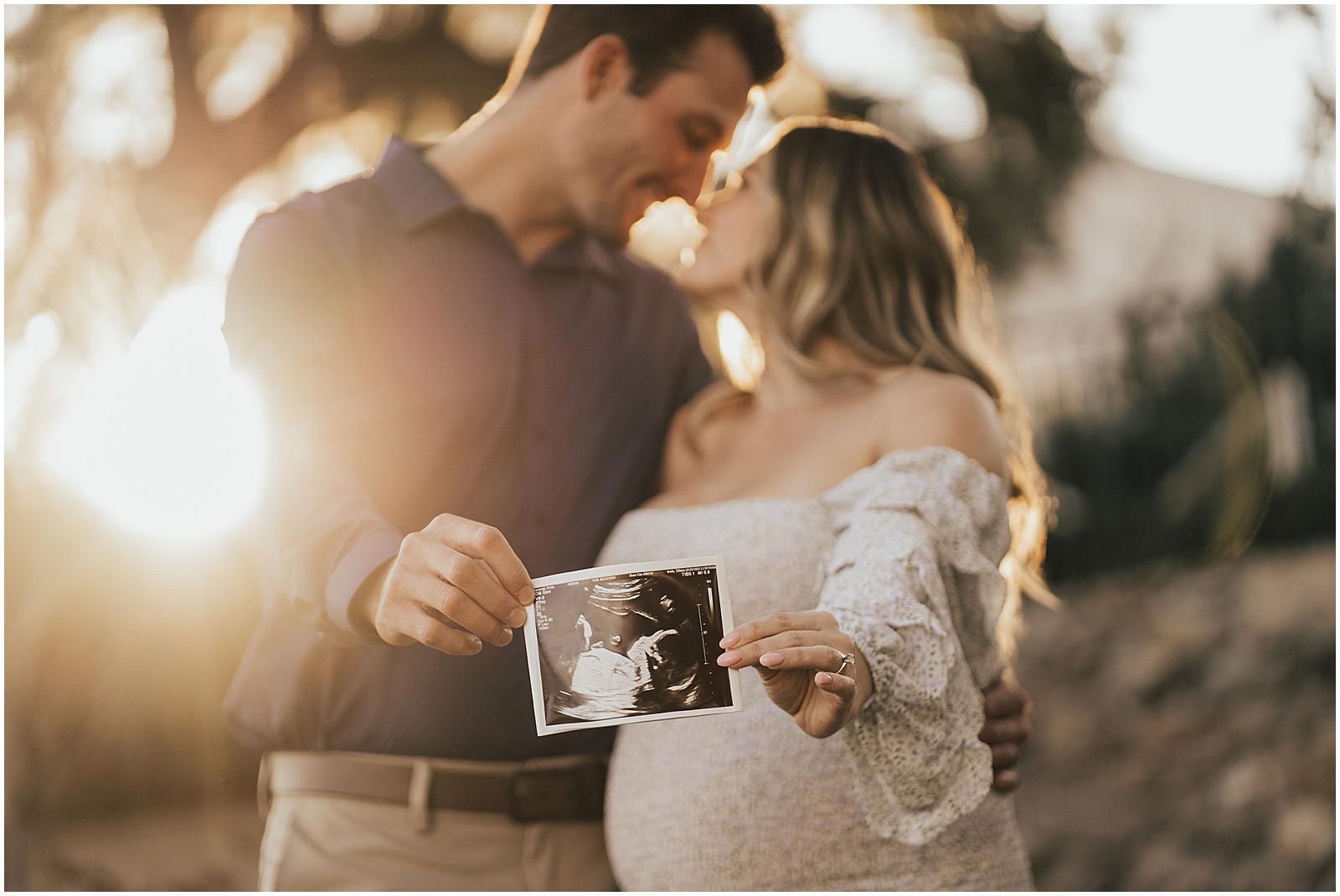 Couple holding sonogram photo with sunset in the background