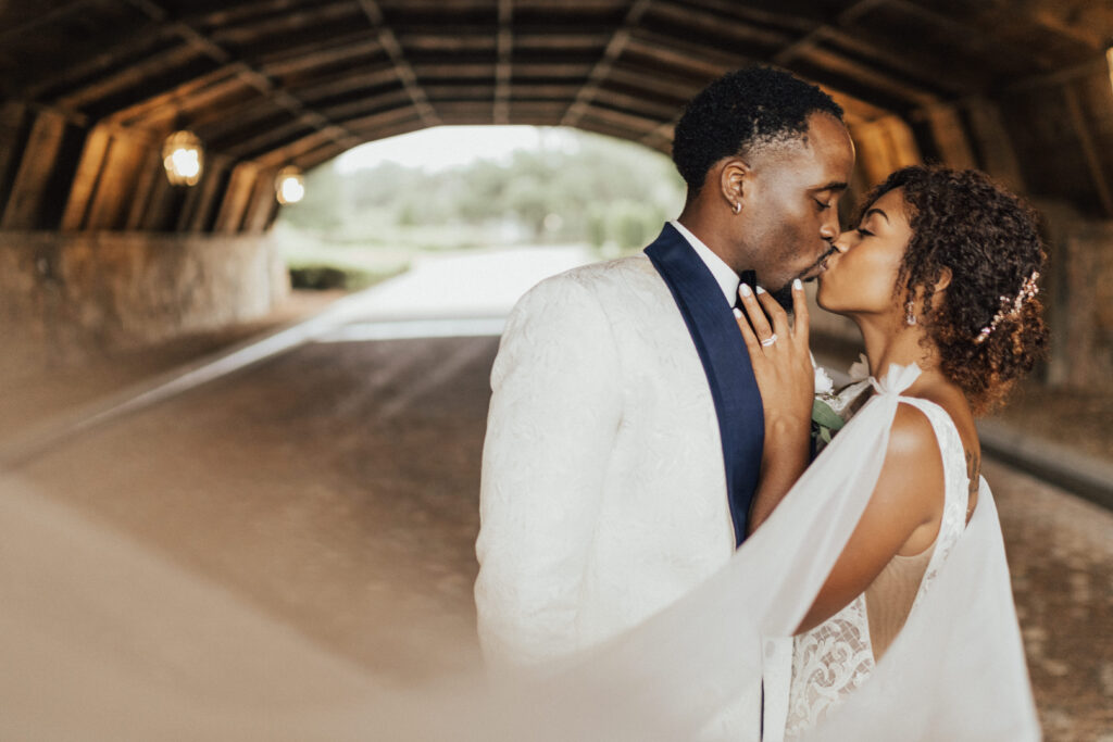 Couple kissing under a bridge in their wedding attire