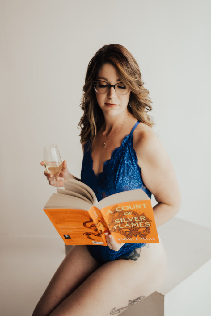 Woman posing in a unique boudoir photoshoot with a book and glass of champagne