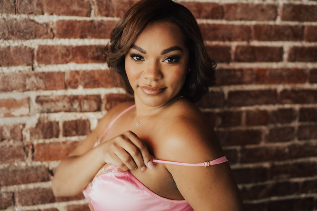 woman posing against wall holding bra strap